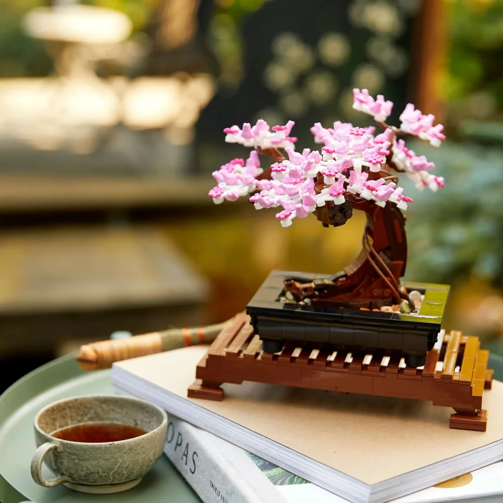 LEGO Bonsai 10281 com folhagem rosa, posicionado em uma estante, reforçando o conceito Home Décor e Zen.