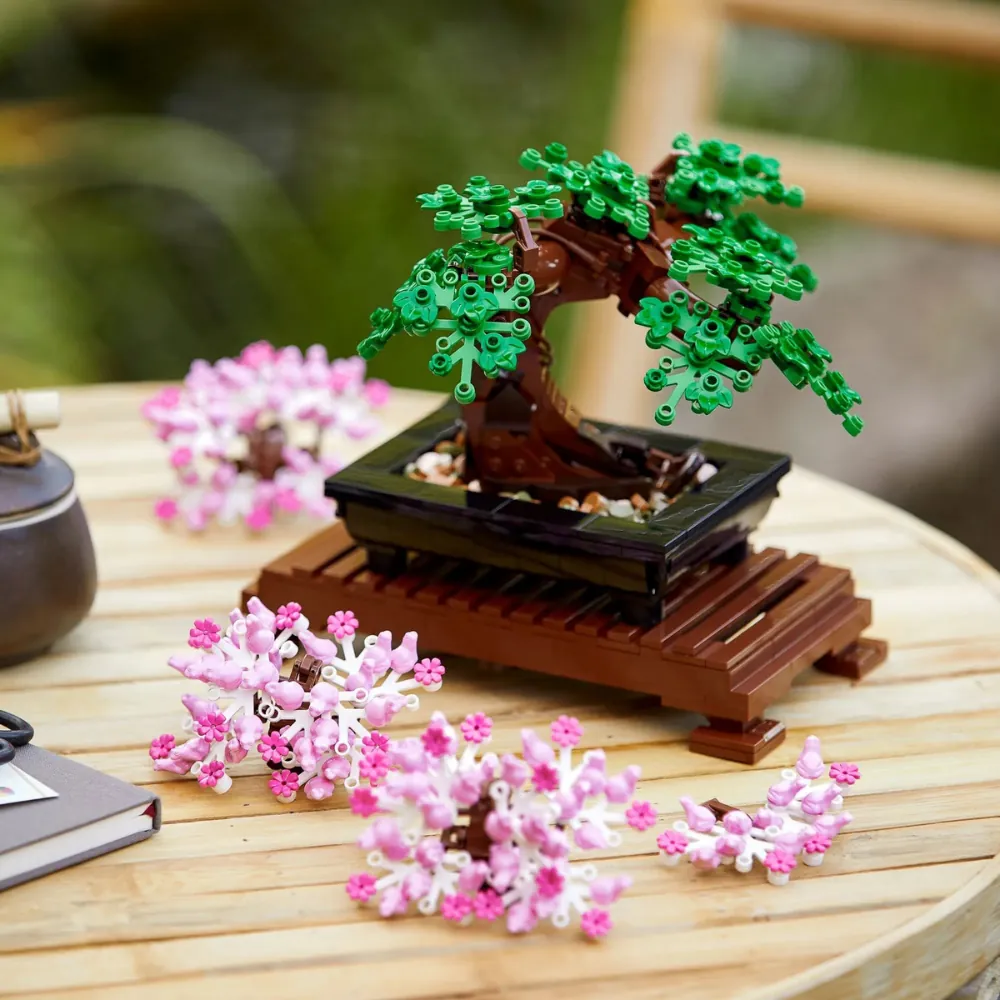 LEGO Bonsai 10281 em folhagem verde com todas as peças rosas de Sakura dispostas ao lado, mostrando o recurso 2 em 1.