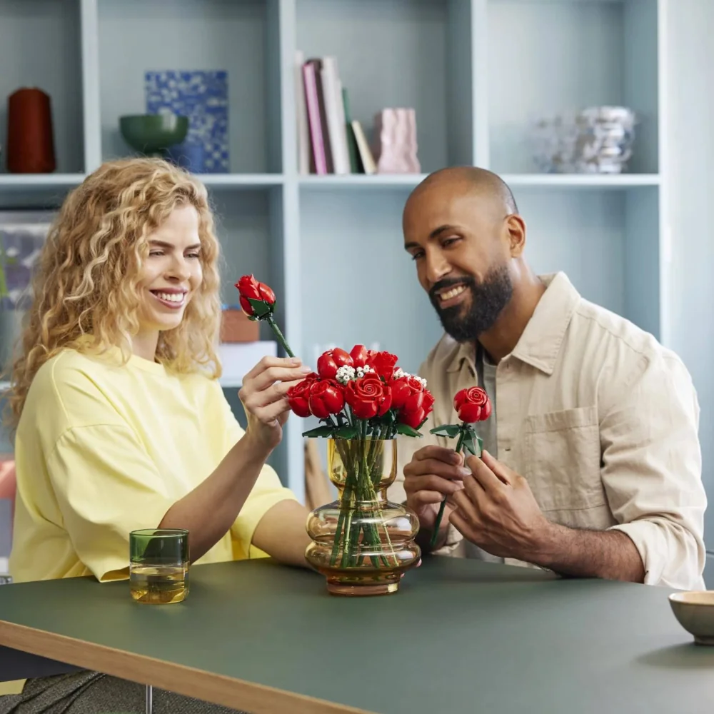 Duas pessoas sorrindo enquanto decoram um vaso com o buquê de flroes.