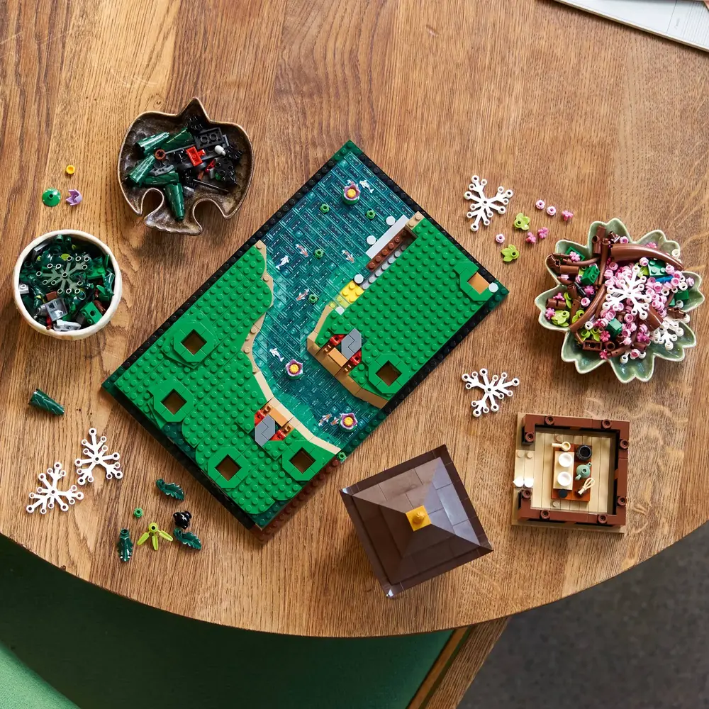 Imagem do LEGO Jardim Tranquilo 10315 mostrando a base modular verde com a casa de chá e ponte vermelha em construção, rodeada por peças de flores e cascalho.